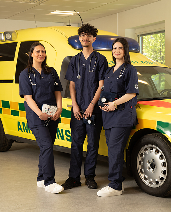 Tre vårdelever står framför ambulans.